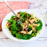 Bacon spinach salad severed on a white plate with ponzu vinaigrette being picked up with a fork.