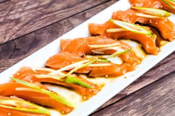 Japanese style salmon carpaccio sashimi in topped with green onions and sliced ginger served in a citrus soy sauce and sesame oil sauce.