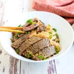 Japanese steak donburi being picked up with a pair of chopsticks.