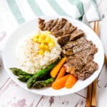 Japanese pepper steak served on a plate with rice, corn, carrots and asparagus.