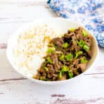 Garlic beef stir fry on top of rice topped with green onions.