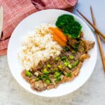 Japanese garlic butter steak served on a plate with fresh rice topped with green onions.