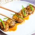 Homemade teriyaki scallops being picked up with chopsticks.