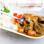 Japanese beef curry served on a plate over rice being scooped up with a spoon.