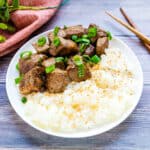 Soy garlic beef cubes served on top of a bed of rice topped with green onions.