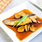 Soy glazed black cod topped with green onions served on a plate.