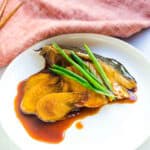 Soy glazed hamachi yellowtail topped with green onions served on a plate.