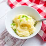 Japanese mashed potato served in a bowl topped with green onions being picked up with a spoon.