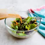 Soy sauce salad dressing being poured onto a green salad.