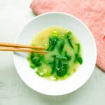 Spinach being picked up with chopsticks from miso soup.