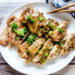 Yuzu grilled chicken topped with green onions served on a plate.