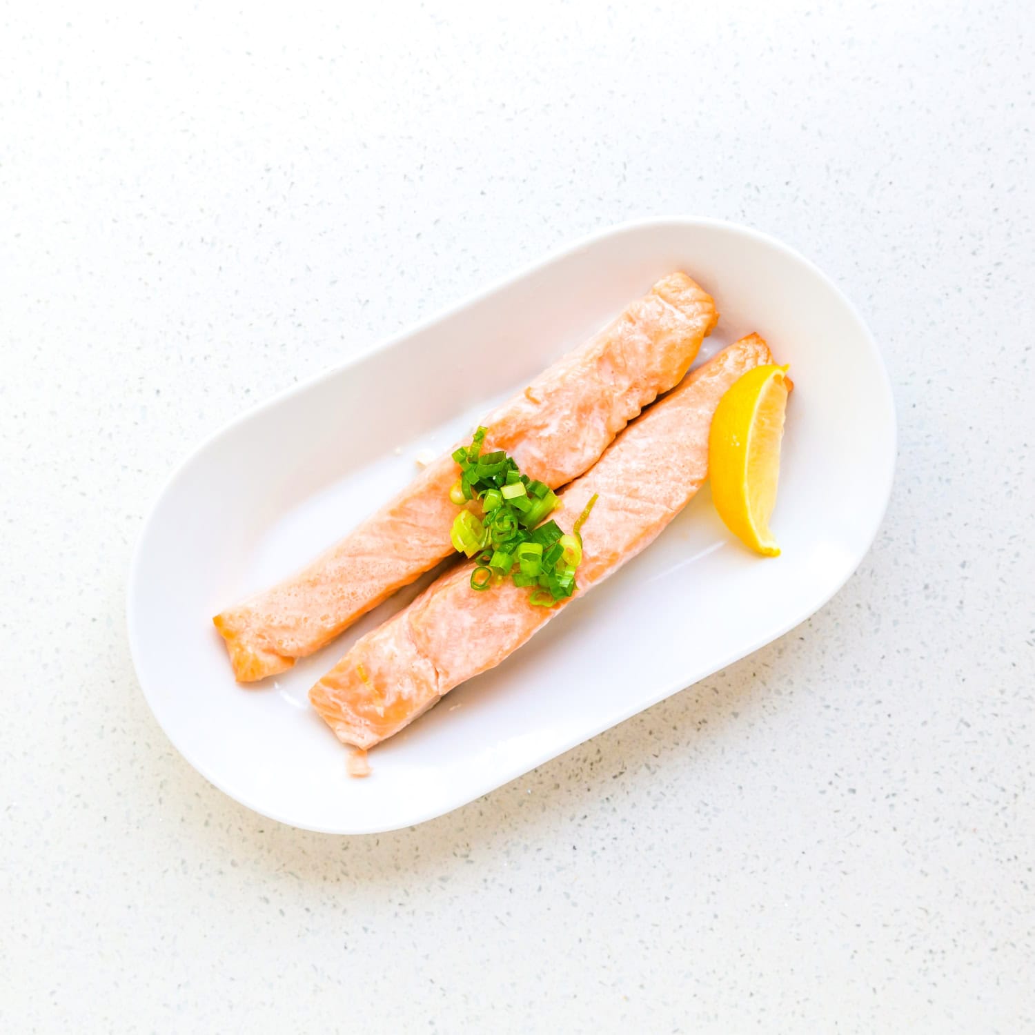 Oven oven roasted salmon strips on a plate with green onions on top. 