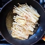 Enoki mushrooms being simmer in a pan.