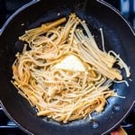 Enoki mushrooms being simmer in a pan.