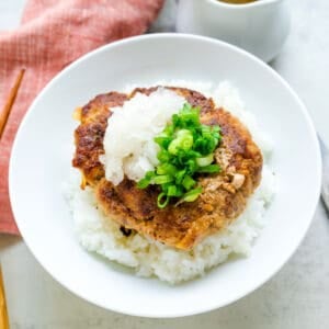 The Japanese burger is served over rice in a bowl, drizzled with Japanese Japanese sauce and topped with scallions.